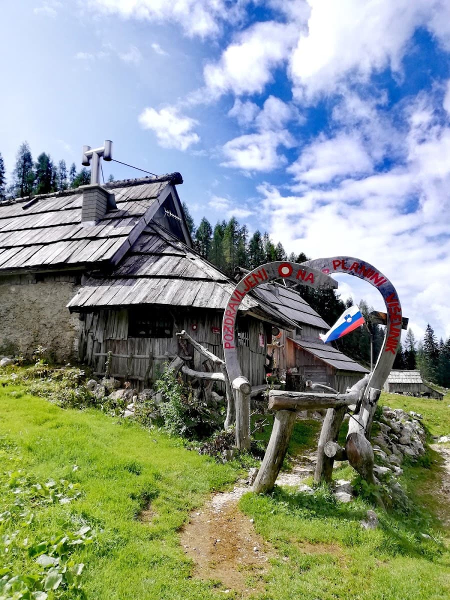 Rustic wooden mountain hut with Slovenian flag under blue sky with clouds