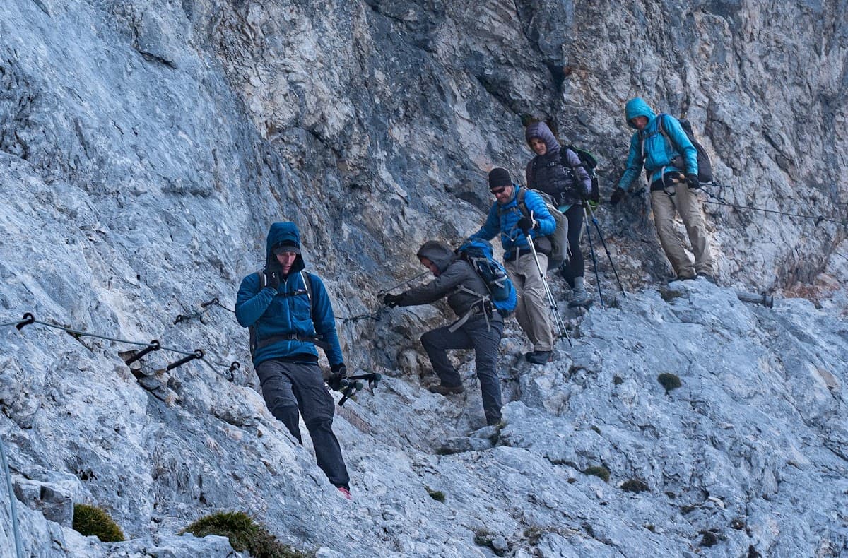 Hikers ascending steep rocky mountain face using fixed cables on a via ferrata route.