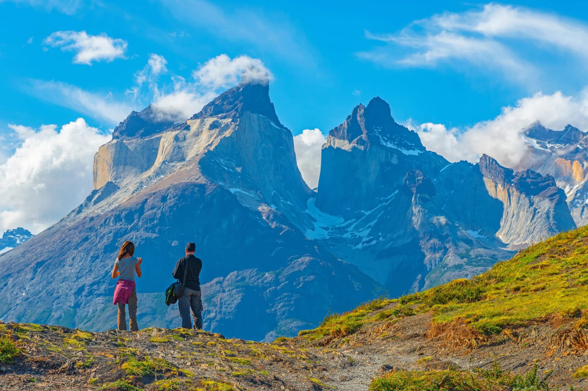 Two tourist, a man and a woman, looking upon a viewpoint of the Andes peaks of Cuernos del Paine, Torres del Paine national park, Puerto Natales, Patagonia, Chile.