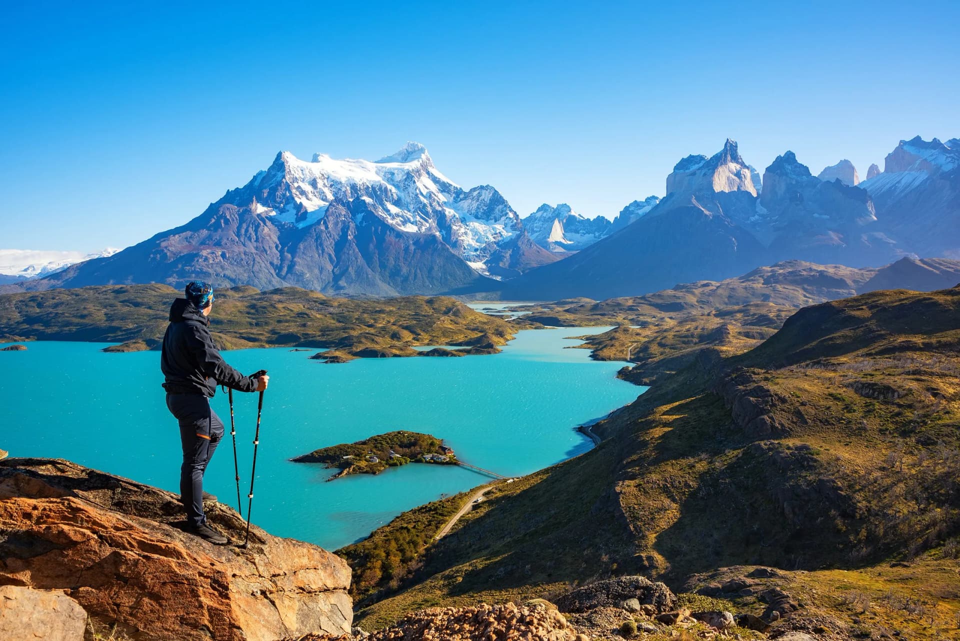 Hiker with poles overlooking turquoise Lake Pehoé and snow-capped mountains in Torres del Paine.