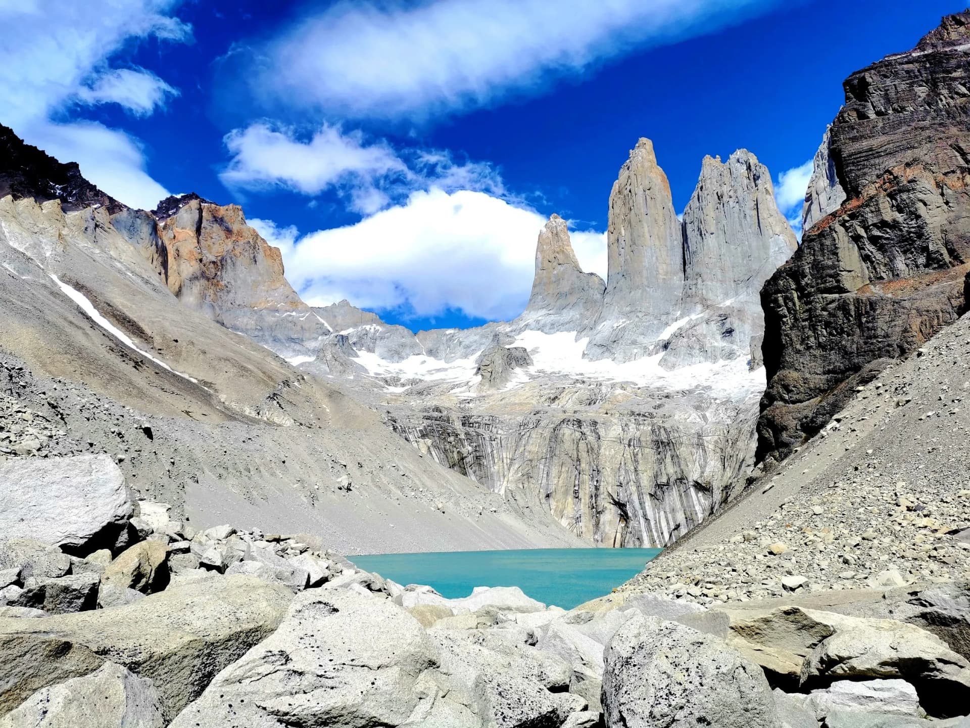 Jagged granite peaks above turquoise glacial lake with snow and bright blue sky