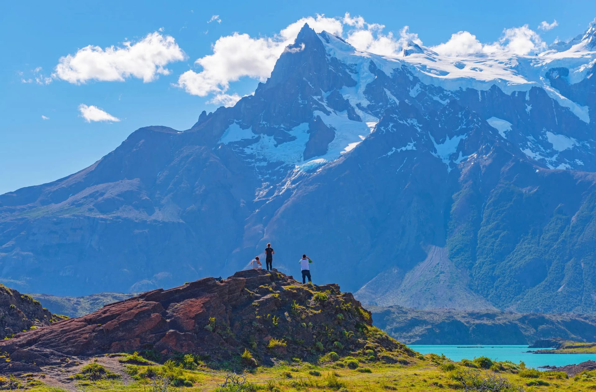 Hikers observing snow-capped mountains above turquoise water at Lake Nordenskjold.