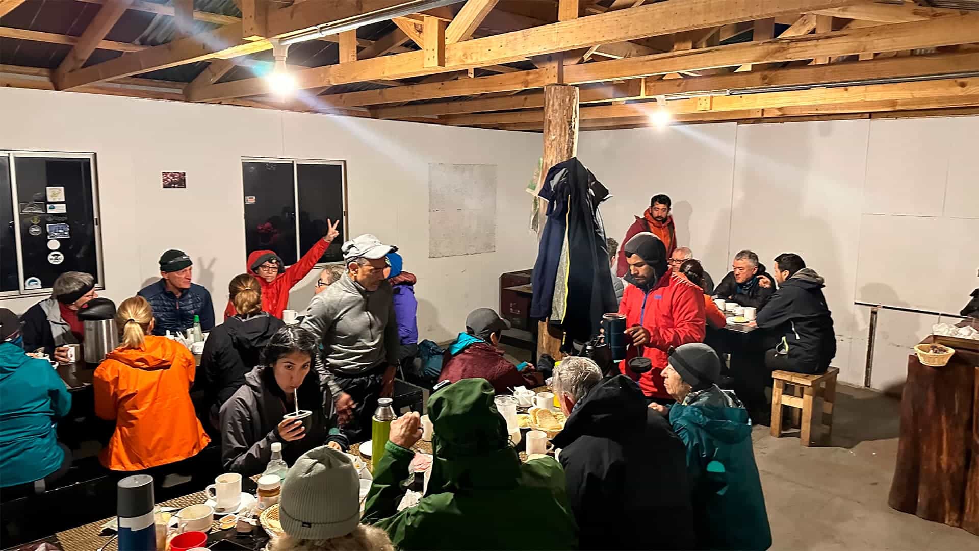 Group of hikers dining indoors in a rustic lodge with exposed wooden beams.