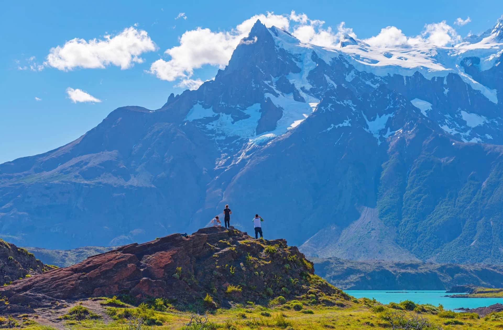 Hikers observing snow-capped mountains above turquoise water at Lake Nordenskjold.